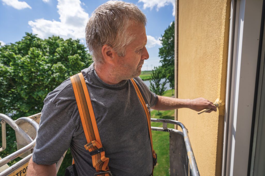 Schilder controleert het buitenschilderwerk aan een gevel